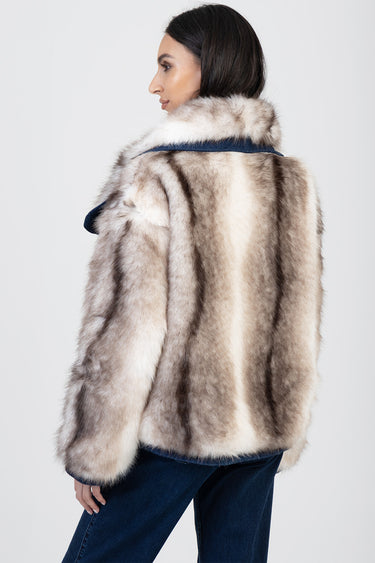 woman wearing a thick beige and cream faux fur jacket seen from the back with blue jeans