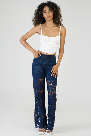 model standing in a white ruched crop top with thin straps and navy wide leg jeans featuring floral lace panels from knee