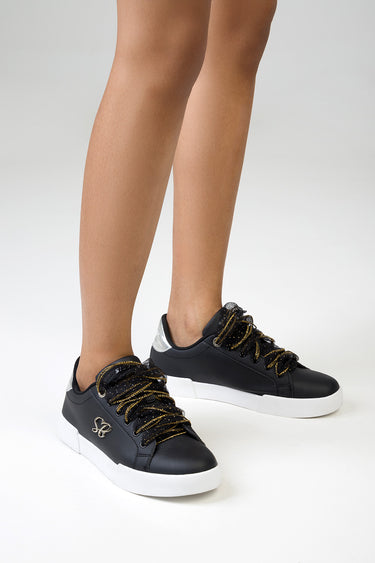 black sneakers with gold glitter laces and white soles on a model's legs