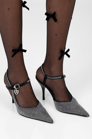 legs wearing sheer black stockings with small dot pattern and black bows, paired with rhinestone adorned pointy heels