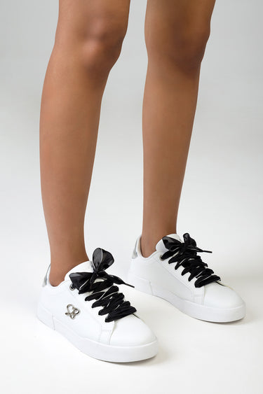 pair of white sneakers with black satin laces tied in bows and a small silver heart logo on the side