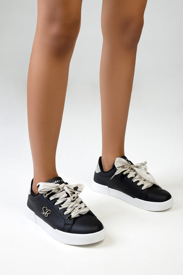 black sneakers with white rubber soles and beige satin laces, with a small logo charm on the side