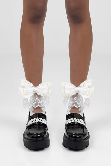 legs in white lace ankle socks with ivory frill and white bows, worn with glossy black loafers
