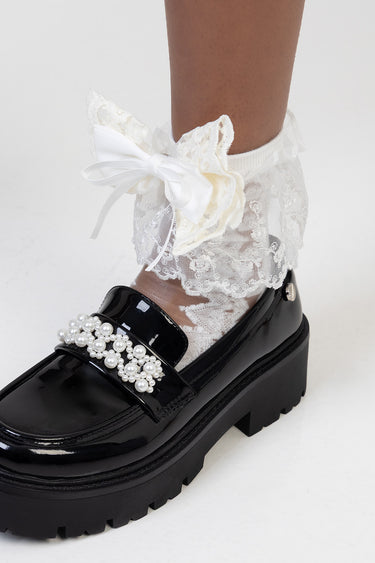white lace ankle sock with a satin bow, paired with a black patent loafer featuring pearl embellishment