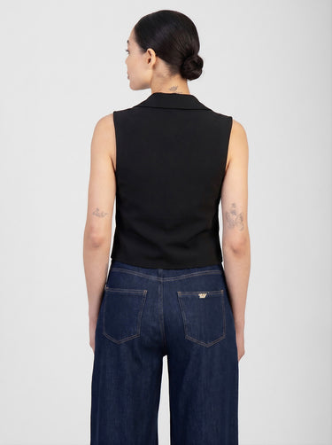 black sleeveless waistcoat with a collar worn over dark blue denim jeans, back view