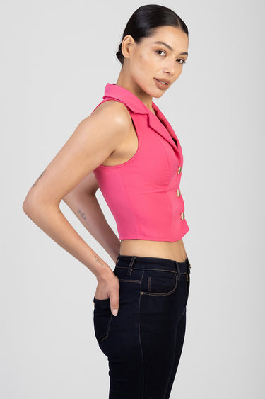 woman in bright pink sleeveless waistcoat with gold buttons and collar, paired with dark denim jeans, side profile