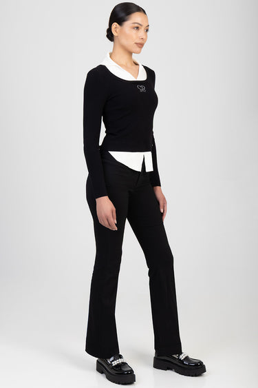 model wearing a black knit top with white collar and hem, black bootleg trousers, and shiny black loafers with chain