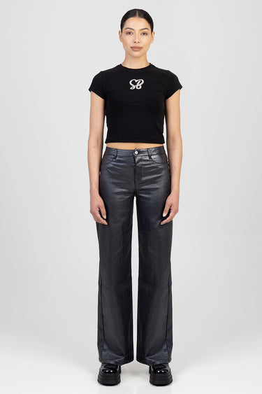 woman wearing a black cropped t-shirt and metallic dark grey wide leg pants, standing.