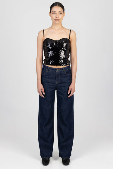 woman wearing black sequin crop top with thin straps and dark blue wide leg jeans in studio