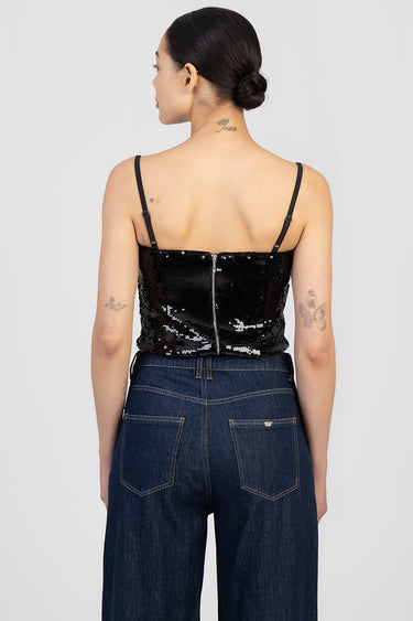 woman wearing a black sequin corset top with thin adjustable straps and a back zipper, paired with dark wash jeans