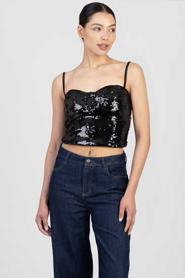 woman wearing a black sequin crop top with thin straps, paired with dark high waisted jeans