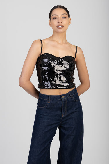 woman wearing a black sequin crop top with spaghetti straps and dark blue wide leg jeans
