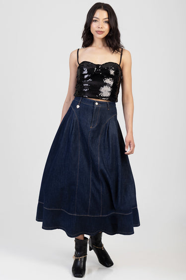 woman wearing a dark denim A-line skirt with contrast stitching and pockets, paired with a black sequin crop top and ankle
