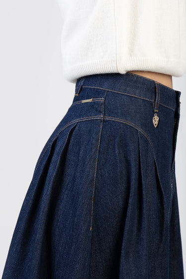 close up of a dark blue denim skirt at the waist with pleated panels and contrast stitching, tiny heart charm on a belt