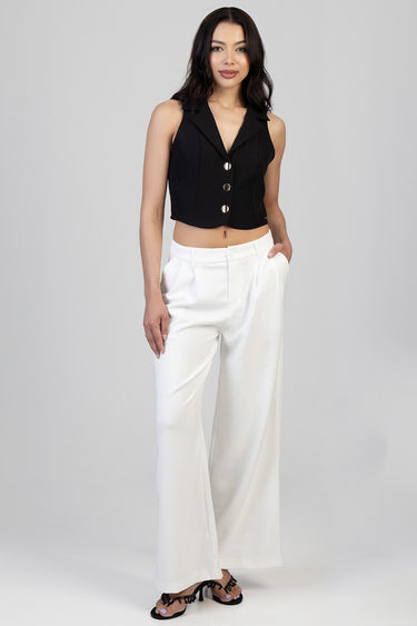 model wearing a black sleeveless cropped blazer with gold buttons and white wide leg trousers, by Blue Jean Traders