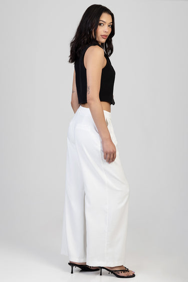 woman in black sleeveless top and white wide leg trousers seen from the side