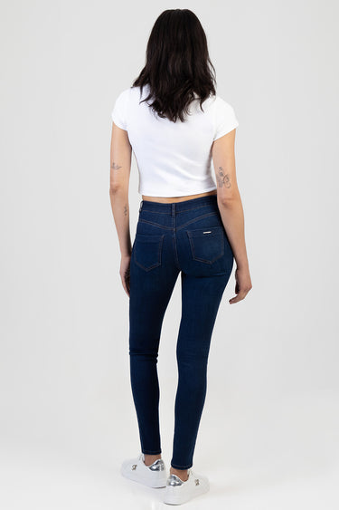 back view of a woman in dark blue skinny jeans by blue jean traders, a white cropped t shirt, and white sneakers with