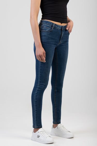 woman wearing dark blue skinny jeans with copper stitching, black top, and white sneakers, side view