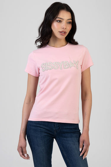pink short sleeve top with silver glitter lettering across the front worn by a model in dark blue jeans