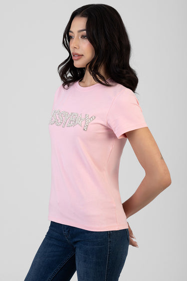 woman wearing a light pink short sleeve crew neck t shirt with silver glitter lettering across the chest, paired with dark