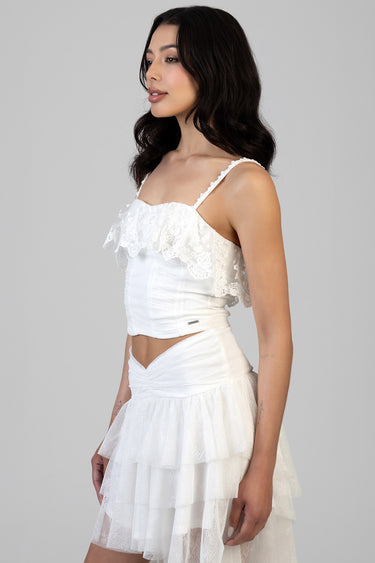 model in a white lace crop top with ruffled overlay and a tiered white lace skirt by blue jean traders