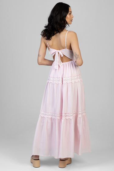 woman wearing a light pink maxi dress with lace panels and a back bow, back view