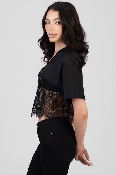 woman in a black boxy short sleeve top with lace overlay and studded embroidery, side profile
