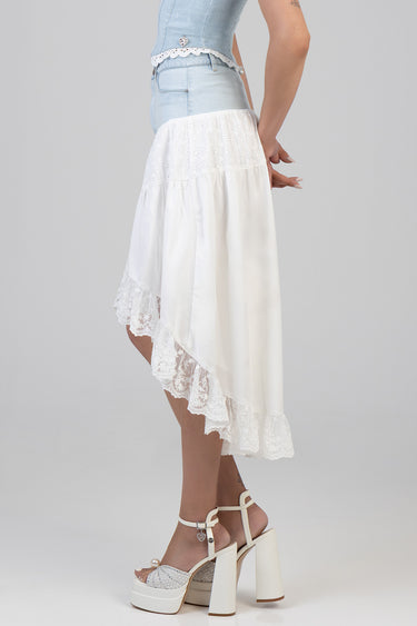 side view of a model wearing a white high low skirt with lace trim, paired with a light wash denim top and white platform