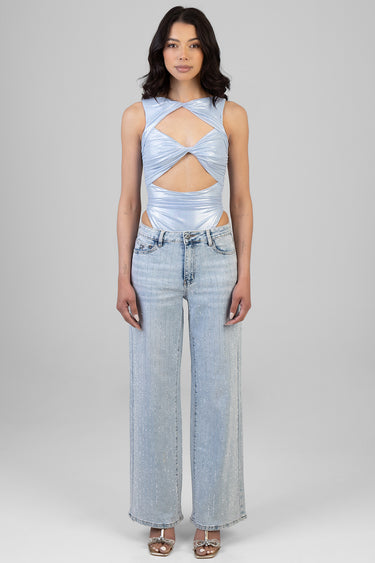 woman in light blue metallic cutout bodysuit with twisted front, paired with light wash jeans.