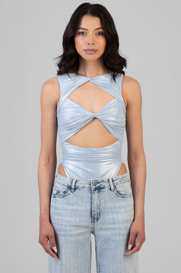 woman in a light blue metallic sleeveless bodysuit with crisscross twist and midriff cutouts, paired with light wash jeans