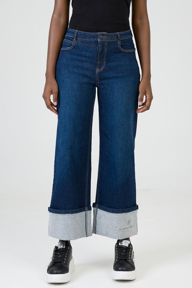 woman wearing dark indigo wide leg jeans with rolled cuffs revealing lighter denim, black top and black sneakers, brand