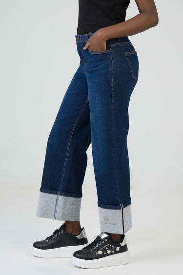 side view of a person wearing dark blue wide leg jeans with rolled cuffs and black sneakers