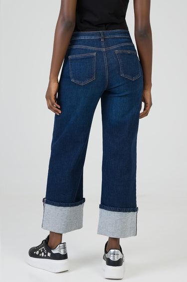 back view of a woman in wide leg dark blue denim jeans with rolled cuffs and contrast stitching with black sneakers