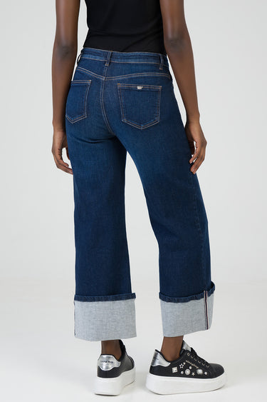 rear view of a person in blue wide-leg jeans with rolled cuffs and back pockets featuring a small logo patch