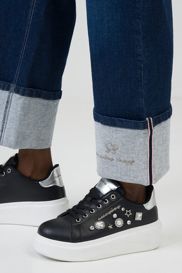 dark blue wide leg jeans with light folded cuffs and a subtle embroidered logo at the hem, paired with black platform