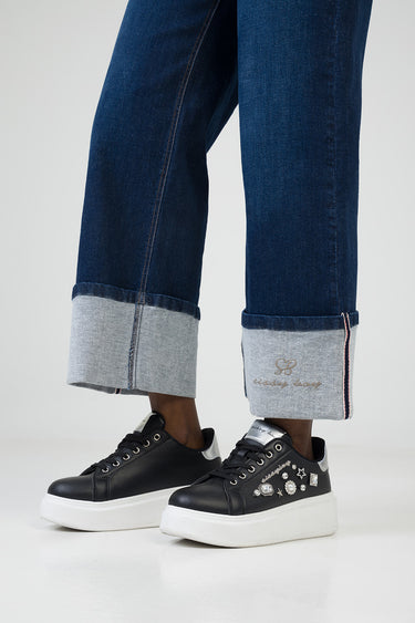 dark blue wide leg jeans with rolled cuffs showing lighter denim, paired with black platform sneakers embellished with