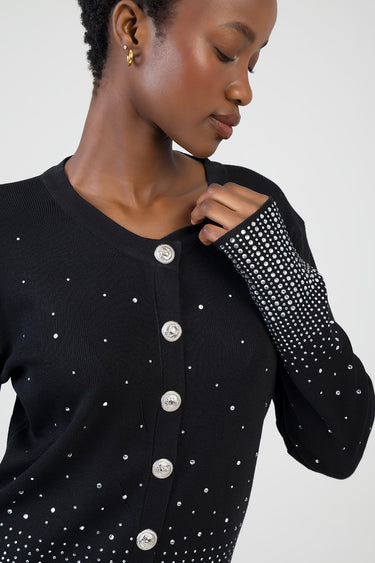 woman wearing a black knit cardigan with silver rhinestones across the body and a sparkling embellished sleeve, buttoned