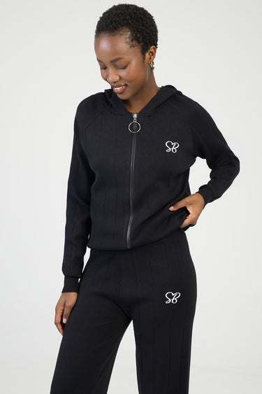 woman wearing a blue jean traders black knit zip jacket with hood and ring pull, paired with matching pants featuring white