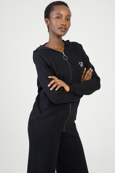 woman wearing a black knit jacket with hood, full front zipper, and ribbed cuffs and hem, white logo on the chest