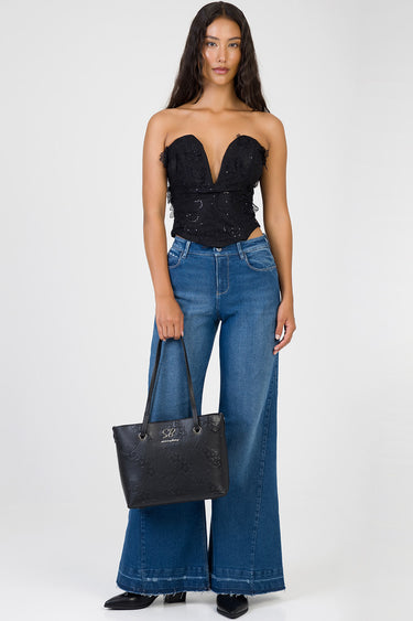 model in strapless black lace corset top with blue wide leg jeans and a black handbag