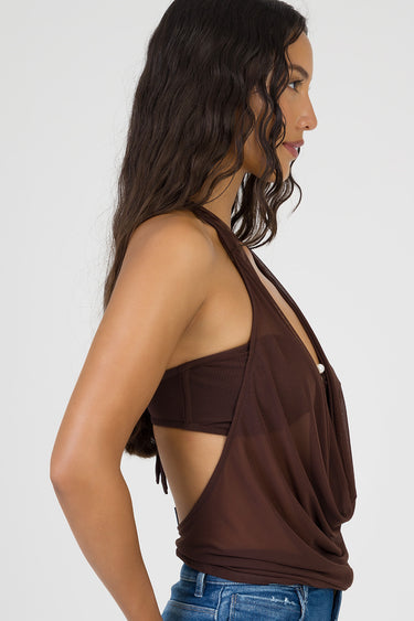 woman in chocolate brown halter top with draped front and sheer overlay, paired with blue denim jeans