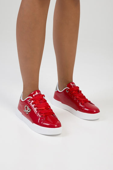 red patent sneakers with white sole and red laces on a model's feet featuring a silver side emblem