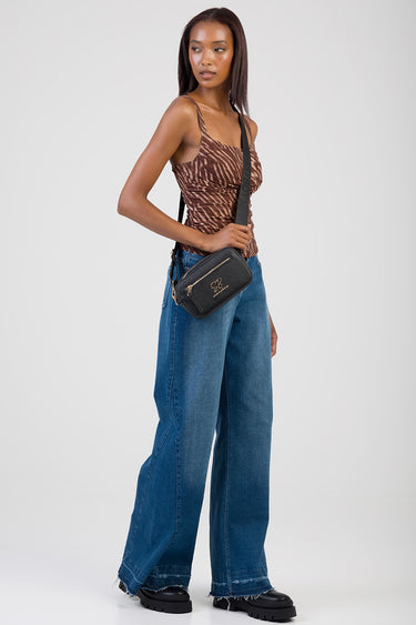 woman wearing a brown patterned tank top and wide leg jeans with a black crossbody bag featuring gold zippers and a