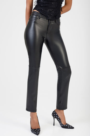 model wearing black leather look stove pipe jeans with seam panels and a high waist, paired with black patterned high heels