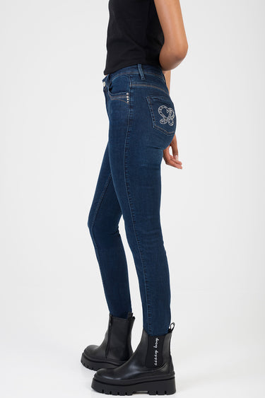 woman wearing dark blue skinny jeans with rhinestone back pocket detail and black boots, side view