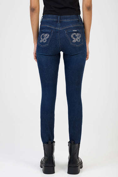 back view of dark blue skinny jeans with rhinestone floral pockets and belt loops, paired with black boots