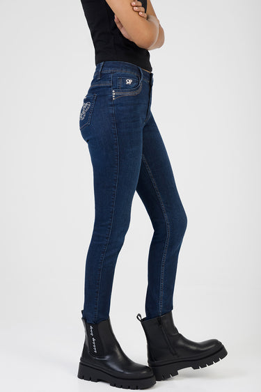 side view of a model wearing dark blue skinny jeans with an embroidered back pocket and a small front pocket logo, paired
