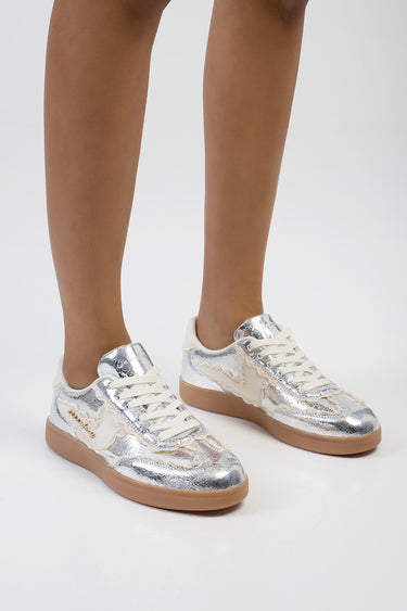 Blue Jean Traders sneakers with silver metallic uppers, cream laces and tan gum sole on a model's feet