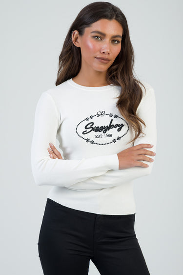 woman models a white knit long sleeve top with a black circular logo on the chest