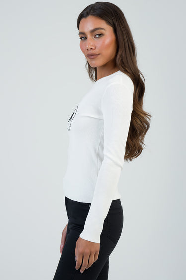 side view of a woman in a white knit long sleeve top and black pants
